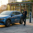 Homme utilisant une tablette près d'une voiture électrique Mercedes en charge sur un parking urbain au coucher du soleil.
